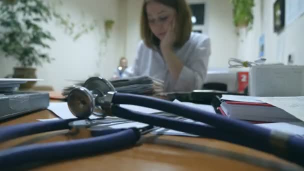 Jonge verpleegster werkt op kantoor, schrijft medische dossiers, stethoscoop op de voorgrond. Vrouwelijke dokter die een recept schrijft in een ziekenhuis. Gezondheidszorgconcept. Sluiten. — Stockvideo