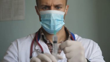 Koruyucu maskeli bir doktorun portresi şırıngadan sıvı boşaltıp üzerine vuruyor. Hastane çalışanı enjeksiyon için ilaç hazırlıyor. Tıbbı test eden bir doktor. Aşı ve COVID-19 kavramı