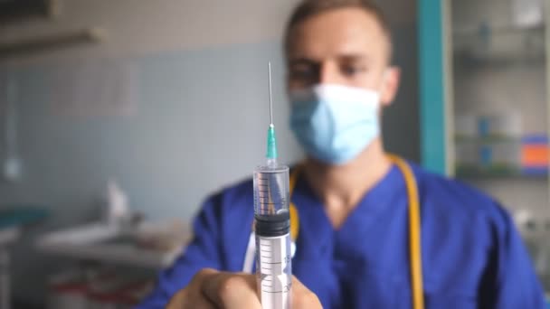 รูปภาพของแพทย์ในหน้ากากป้องกันการเทของเหลวจากเข็มฉีดยา พนักงานโรงพยาบาลชายเตรียมยาสําหรับฉีดยา พนักงานทางการแพทย์ทดสอบยา แนวคิดการฉีดวัคซีนและการดูแลสุขภาพ ปิดขึ้น — วีดีโอสต็อก