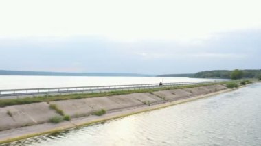 Motosikletlinin göl kenarındaki yolda motosikletiyle yarışırken çekilmiş bir fotoğrafı. Adam yaz günü baraj yolunda bisiklet sürüyor. Modern spor motosikletle nehir köprüsünün üzerinden uçuyor. Üst görünüm