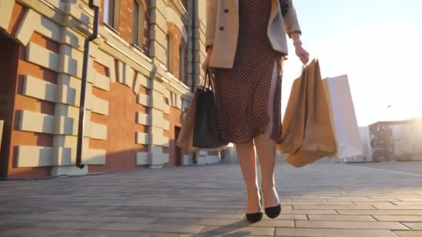 Elegant woman carries full paper packets walking along urban square. Female customer in beautiful dress holds shopping bags going at sidewalk after purchases. Concept of seasonal sales. Dolly shot — Video