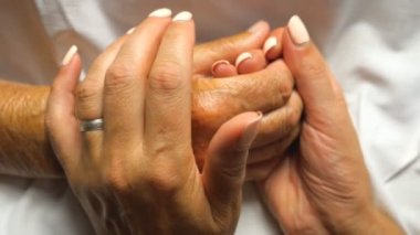 Genç bir kadın annesinin şefkatini ya da sevgisini göstererek elini nazikçe okşuyor. Yatakta yatan yaşlı bir annenin kırışık avuç içini rahatlatan kızı. Kız, eski ailesine destek oluyor. Üst Görünüm Kapat