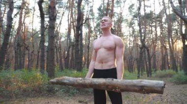 Kaslı adam ağır ağırlık antrenmanı kaslarını kaldırıyor. Gün batımında ormanda çalışan güçlü ve dayanıklı bir adam. Sporcu büyük kütükleri kullanarak dışarıda egzersiz yapıyor. Spor ve aktif yaşam tarzı konsepti. Dolly vurdu.