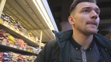 Süpermarkette elinde tramvayla yürüyen genç bir adamın portresi. Dükkâna ürün almaya giden bir adam. Alıcı üretim departmanından yiyecek seçer. Bakkalda günlük alışveriş kavramı. Kapat.
