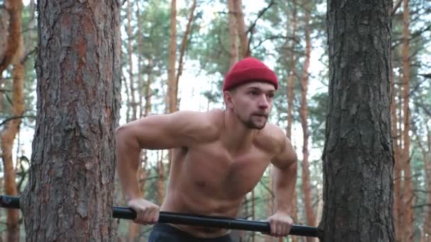 強く、筋肉質の男は森の水平方向のバーでプッシュアップを行う。ハーディ・スポーツマンは自然に取り組んでいる。アスレチック男のトレーニング屋外。スポーツとアクティブライフスタイルの概念。スローモーションを閉じます — ストック動画