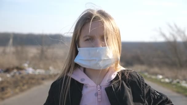 屋外に立って医療面マスクを持つ少女の肖像画。外部からのウイルスから保護マスクを身に着けている悲しい女性子供。コロナウイルスとパンデミックからの健康と安全の生活の概念。閉じろ! — ストック動画