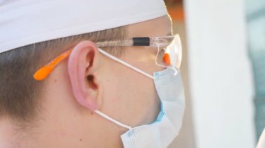 Coronavirus için kan örneği olan test tüplerine bakan doktor profili. Koruyucu gözlüklü erkek doktor kan örneklerini COVID-19 virüsüne test ediyor. Salgından korunan sağlık ve güvenlik kavramı