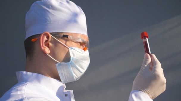 Medico che esplora la provetta con il campione di sangue al coronavirus. Medic con guanti protettivi e occhiali di visualizzazione e test di analisi del sangue a COVID-19. Concetto di salute e sicurezza vita da pandemia — Video Stock