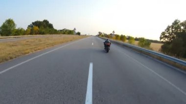 Güneşli bir sonbahar gününde otoyolda motosiklet süren motosikletliyi takip edin. Motosikletli, kır yolunda motosikletiyle yarışıyor. Yolculuk sırasında bisiklet süren bir adam. Yolculuk kavramı. Hava görüntüsü