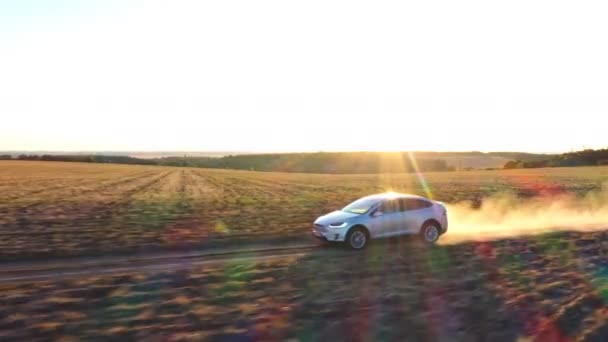 Aerial shot of electrical car moving on off-road route leaving dust trail behind. Ecology friendly auto on electric charge driving along rural road. Scenic sunset landscape at background. Side view — Stock Video