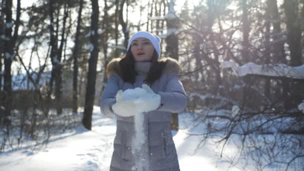 Młoda szczęśliwa kobieta w zimowych ubraniach rzucając garść śniegu i ciesząc się spadającymi płatkami śniegu. Atrakcyjna dziewczyna bawi się śniegiem w piękny zimowy dzień. Koncepcja urlopu zimowego. Powolne mo Zamknij się — Wideo stockowe