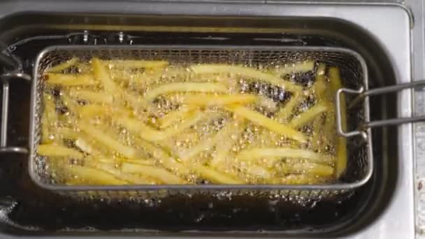 Smakliga pommes frites tillagas i fritös i köket. Krispig potatis steks i het kokande olja i köket. Processen att göra snabbmat. Begreppet matlagning. Ovanifrån Slow motion — Stockvideo