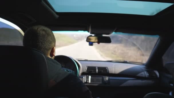 Vista dal sedile posteriore sul giovane guida una macchina sulla strada vuota. Un tizio cavalca nel suo moderno SUV attraverso la campagna. Turismo maschile viaggia sulla sua auto. Concetto di viaggio. Chiudere rallentatore — Video Stock