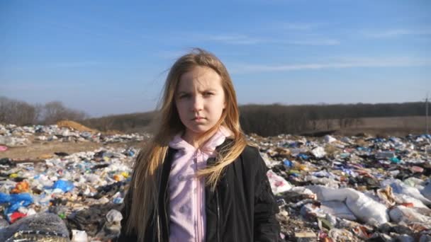 Πορτραίτο του μικρού γυναικείου παιδιού κοιτάζει στην κάμερα στο θολό φόντο της βρώμικης χωματερής. Ένα μικρό σοβαρό κορίτσι στέκεται στη μάντρα στην εξοχή. Έννοια του προβλήματος περιβαλλοντικής ρύπανσης — Αρχείο Βίντεο