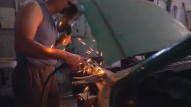 Koruyucu maske takan profesyonel bir tamirci. Garajda ya da atölyede çalışan tamirci. Adam servis aracına çarpmış. Sıcak kıvılcımlar uçuşuyor. Araba tamiri ve bakım konsepti