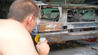 Atölyede elektrikli aletle araba cilalamak. Otomobili tamir etmekte ustaymış. Tamirci eski araba gövdesini öğütücüyle öğütüyor. Garajda servis yapan bir adam var. Arka plan