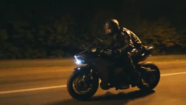 헬멧을 쓴 젊은이가 저녁 거리에서 현대 흑인 스포츠 오토바이를 타고 빠르게 달리고 있습니다. 오토바이가 밤에 빈 도로에서 자신의 오토바이를 경주. 바이크 운전하는 남자. 자유와 취미의 개념. 닫아 — 비디오