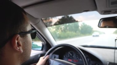 Otobanda güneş gözlüklü tanınmayan bir adam araba kullanıyor. Otomobili kontrol ederken yola çıkmak isteyen kendine güvenen genç adam. Araç kuaföründen arka manzara. Yolculuk kavramı. Yavaş çekim