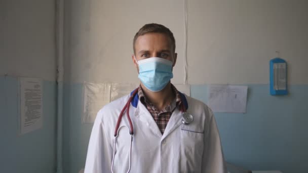 Positive doctor taking off protective mask and smiling. Portrait of happy physician wearing medical uniform posing in hospital office. Cheerful hospital employee with joy emotions on face. Close up — Wideo stockowe