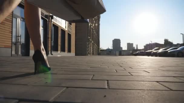 Female feet in black shoes on high heels stepping at sidewalk. Girl going with packets at city square after purchases. Hands of young woman carry shopping bags walking along urban street. Rear view — Stock Video