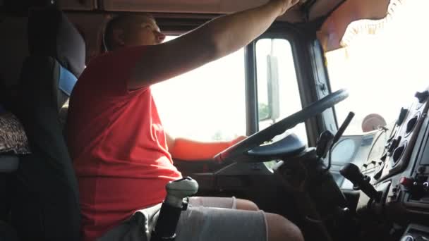 Kierowca ciężarówki jedzie przez wieś i rozmawia przez radio. Kierowca ciężarówki rozmawia przez krótkofalówkę podczas jazdy samochodem po wiejskiej drodze. Logistyka i koncepcja transportu. Zwolniony ruch — Wideo stockowe