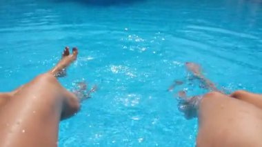 Havuzun kenarında oturan ve ayaklarını suya sokan genç kadınlar. İnce bronzlaşmış bacakları olan iki kız lavabonun yanında dinleniyor. Hanımlar tatilin tadını çıkarıyor. Yaz tatili kavramı. Kapat.