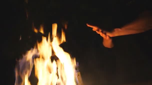 Schlechter Blick auf junge Touristen, die sich nachts vor einem offenen Lagerfeuer die Hände reiben. Der Mensch wärmt seine Arme durch ein Feuer aus Metallkesseln vor schwarzem Hintergrund. Konzept von Wärme und Ruhe — Stockvideo