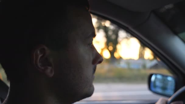 Профиль красивого мужчины, проезжающего на машине по сельской местности на закате. Молодой уверенный парень внимательно смотрит на дорогу во время контроля авто. Концепция путешествия. Вид сбоку Медленное движение — стоковое видео