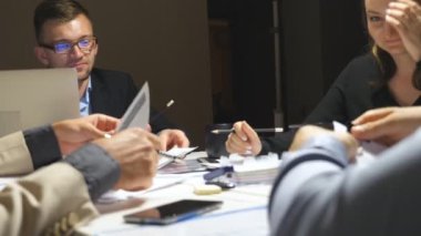 Ofiste kurumsal proje için iş ekibi planlama stratejisi. Genç iş arkadaşları masada oturuyor ve belgeleri inceliyorlar. İş adamları iş gününün sonunda finansal grafikleri kontrol eder. Yakın çekim