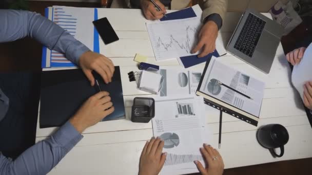 Vue de dessus mains masculines et féminines de collègues analysant les rapports financiers au bureau. Équipe d'affaires assise à la table et examinant les documents. Coworkers vérifiant les graphiques à la fin de la journée de travail — Video