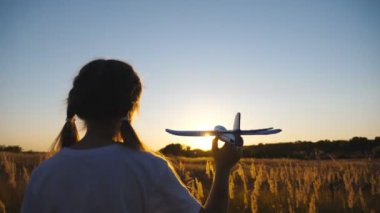 Küçük kız çayırların arasında uçakla oynuyor. Tasasız küçük çocuk arka planda gün batımına karşı oyuncak uçakla sahada yürüyor. Hafta sonunun tadını çıkaran tatlı bir bayan çocuk. Arka görünüm