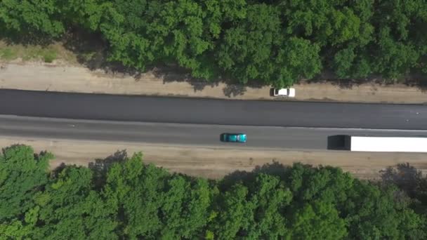 Luftaufnahme eines Autos mit LKW, das auf einer neuen Asphaltstraße durch den Wald fährt. Drohne fliegt über Lastwagen, die Ladung auf Landstraße transportieren. Autoverkehr auf Autobahnen. LKW-Konzept. Ansicht von oben — Stockvideo