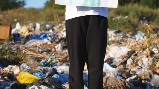 Klein meisje houdt in handen bordje van milieubeweging voor het redden van de aarde. Kleine eco vrijwilliger in beschermende masker pleiten voor natuurbehoud tegen de achtergrond van vuile stortplaats. Kraanschot — Stockvideo