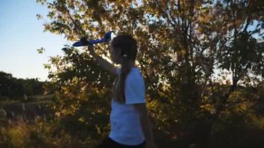 Küçük çocuk kırsalda yürürken uçakla oynuyor. Küçük mutlu kız arka planda güneş ışığına karşı oyuncak uçakla gidiyor. Tasasız çocuk doğayla eğleniyor. Çocukluk hayali konsepti. Yavaş çekim