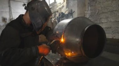 Endüstriyel metal üretiminde kaynakçı metal yapımı. Koruyucu maskeli bir işçi iki çelik detay arasında ortaklık yapıyor. Adam metal parçalarını birbirine kaynaştırıyor. Kapat..