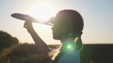 Close up of little kid going with toy plane against sunset at background. Happy small girl plays with airplane walking at countryside. Carefree child having fun at nature. Childhood dream concept.