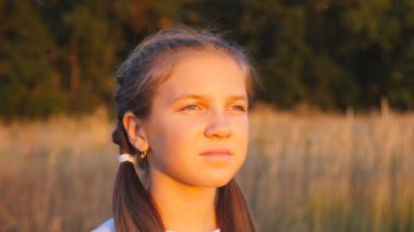 Mutlu gülümseyen kızın portresi çayırda duruyor ve güzel bir akşam gün batımına bakıyor. Yaz günü parlak güneş ışınlarıyla aydınlatan sevimli bir kadın yüzü. Tasasız ve özgür olma kavramı. Kapat..