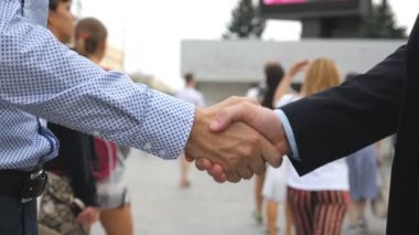Şehir ortamında birbirini selamlayan iki iş adamı. Bulanık şehir geçmişine sahip genç erkek arkadaşlar el sıkışıyor. İş ortaklarının el sıkışması. Yan Görünüm Yavaşça Kapat.