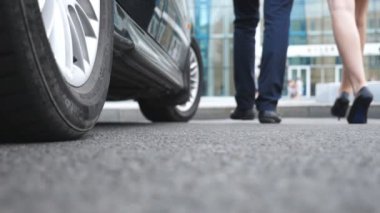 Feet of businessman in black shoes and businesswoman on high heels got out of car and walking in street. Business couple came out of auto and going to work. Blurred motion. Low angle view Slow motion.