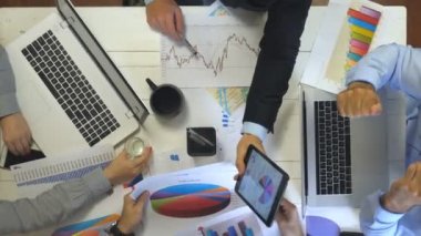 Laptopları ve grafikleri kullanarak verimli çalışan iş adamlarının üst görüntüsü. Moda ofisindeki masada oturan bir grup genç işçi. Yaratıcı ekip geliştirme işiyle meşgul. Yavaş çekim Kapat
