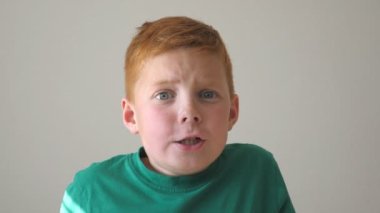 Sevimli yakışıklı çocuk kameraya neşe ve şaşkınlıkla bakar. Kapalı alanda çilli mutlu bir çocuğun portresi. Yüzünde neşe ve şaşkınlık ifadesi olan genç bir çocuk. Yavaş çekim. Yakın çekim..