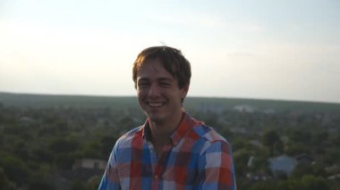 Cityscape arka plan, çatıda oturan genç mutlu adam portresi. Gülüyor ve yüzünde sevinç ifade gösterilen yakışıklı olan. Mutlu bir insan samimi duyguların. Dolly shot ağır çekim yakın çekim.