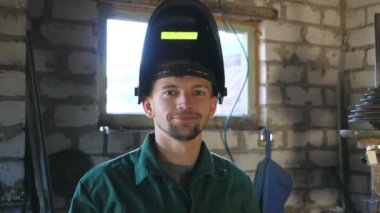 Welder smiling and looking at camera. Portrait of happy man with beard working in his garage or workshop. Close up emotions of male worker with glad expression on face. Slow motion.
