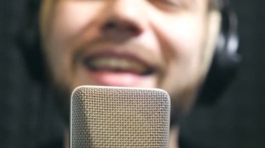 Male singer in headphones singing song into the microphone at sound studio. Young man emotionally recording new melody or song. Working of creative musician. Show business concept. Slow motion.