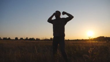 Yaz otlağında kollarını açan mutlu adam. Genç adam gün batımında çim tarlasında muzaffer bir şekilde el kaldırıyor. Erkek güzel doğada dinleniyor. Tasasız ve özgür olma kavramı. Dolly vurdu..