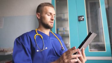 Genç doktor tablet kullanarak hastaya danışıyor. Dijital cihazı tutan ve biriyle konuşan bir tıp çalışanı. Corona salgını sırasında klinikte çalışan bir erkek doktor. Sağlık ve COVID-19 salgın konsepti