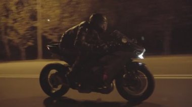 Motorcyclist riding fast on powerful sport motorbike at night road. Male racer in protective moto equipment moving on modern motorcycle at evening city street. Freedom and adventure concept. Close up.