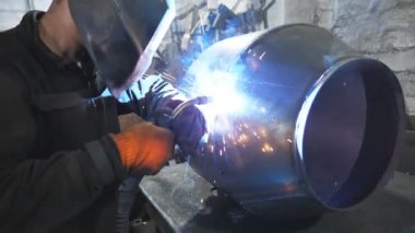 Kaynakçı iki çelik detay arasında ortaklık yapıyor. Adam metal parçalarını birbirine kaynaştırıyor. Metal fabrikasında koruyucu maske kaynak işçisi. Yavaş çekim. Yakın çekim..