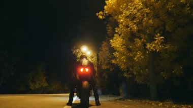 Kasklı ve deri ceketli bisikletçi gece otobanında motosikletinin üzerinde oturuyor ve sürüşe başlıyor. Adam akşam vakti motosiklet sürmeye başlıyor. Özgürlük ve macera kavramı. Arka görünüm.