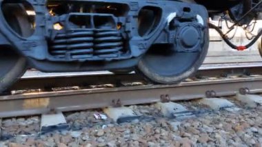 Demiryolu boyunca ilerleyen ve endüstriyel malları taşıyan çelik tren çarkını kapatın. Kamera, taşıma arabalarının kırsal alandan geçtiği endüstriyel lokomotifi izliyor. Kargo taşımacılığı veya teslimatı